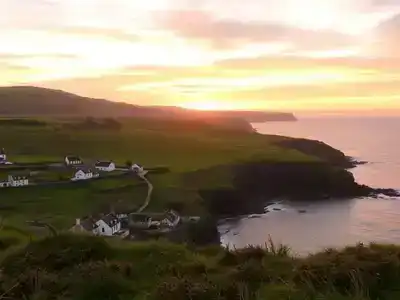 Scenic Donegal coastline with green hills and sunset.
